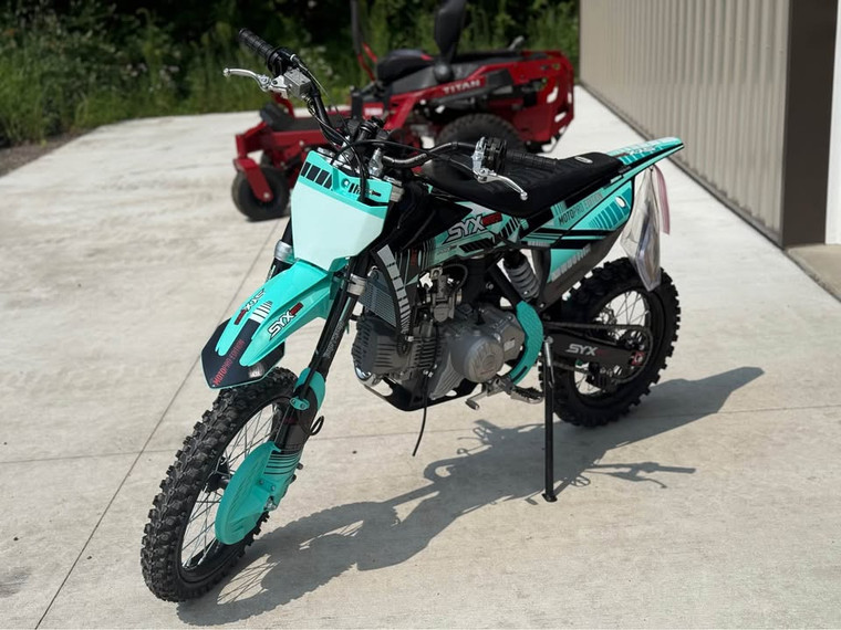 SYX MotoPro PAD190-V2 190cc Pit Bike in one of its two available color options: Red with Grey or Teal with Black. The bike features a sleek and modern design with upgraded plastic kits and a new muffler with a chrome pipe and anti-scalding sheet. The inverted front fork and SX rear shock absorber are prominently displayed, highlighting the bike's advanced suspension system. The heavy-duty black steel rims with deep-teeth pattern off-road tires and hydraulic disc brakes are visible, emphasizing the bike's durability and safety features. The handlebar with a built-in air filter and the SY new forged triple clamp add to the bike's premium feel. The SY V2 double tube cradle frame and SY steel swing arm (knife-shape) are also showcased, underscoring the bike's robust construction. Overall, the image captures the essence of a high-performance, stylish, and durable pit bike ready for any off-road adventure. SYX MotoPro PAD190-V2 190cc Pit Bike in one of its two available color options: Red with Grey or Teal with Black. The bike features a sleek and modern design with upgraded plastic kits and a new muffler with a chrome pipe and anti-scalding sheet. The inverted front fork and SX rear shock absorber are prominently displayed, highlighting the bike's advanced suspension system. The heavy-duty black steel rims with deep-teeth pattern off-road tires and hydraulic disc brakes are visible, emphasizing the bike's durability and safety features. The handlebar with a built-in air filter and the SY new forged triple clamp add to the bike's premium feel. The SY V2 double tube cradle frame and SY steel swing arm (knife-shape) are also showcased, underscoring the bike's robust construction. Overall, the image captures the essence of a high-performance, stylish, and durable pit bike ready for any off-road adventure.