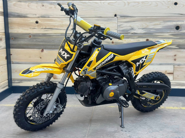 "The Denago MX Yellow Edition pit bike features a 110cc engine with electric start, automatic transmission, and hydraulic disc brakes. Shown with vibrant yellow accents on CNC components, black powder-coated wheels, and aggressive knobby tires, this beginner-friendly bike offers adjustable suspension and foldable levers. Perfect for trails and backyard riding with its 24" seat height."