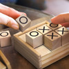 A wooden Tic Tac Toe game with light timber blocks featuring O and X marks, housed in a small timber box.