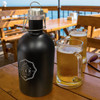 A drink bottle with a matte black finish and a metal cap, accompanied by two glasses of beer on a wooden table.
