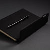 A black A5 notebook with a matching black pen, featuring a subtle logo on the notebook cover.