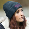 A grey waffle beanie with a branded logo, worn by a person with long hair and a thoughtful expression.
