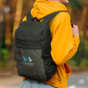 A person wearing a yellow hoodie carries a dark green and grey Campster Backpack with a logo on the front.