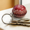 A red cricket ball key ring attached to metal keys, featuring stitched detailing and a logo.