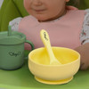 A yellow suction bowl with a matching spoon beside a green drink cup, both featuring a logo.