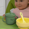 A drink bottle in green with a handle and straw, accompanied by a yellow bowl and spoon. The bottle features a logo.