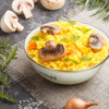 A Bendigo enamel bowl filled with yellow rice, mushrooms, and herbs, surrounded by fresh ingredients on a textured surface.