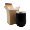 A reusable black coffee cup with a clear lid beside a brown cardboard box. The cup features a metallic base and has a logo.