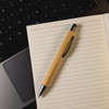 A bamboo stylus pen rests on a blank lined notebook, alongside a laptop keyboard.