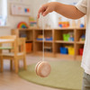 A child's hand holds a wooden yo-yo with a natural finish, dangling on a string in a bright, playful indoor space.