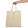 A hand holds a cream-coloured calico bag with short handles, featuring a simple design and no visible branding.