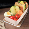 A beige lunch box filled with an apple, a sandwich, tomatoes, a boiled egg, and a tangerine, set on a cork mat.