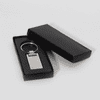 A silver keychain displayed inside a black box. The keychain has a rectangular shape with a polished finish.