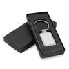 A rectangular metal keychain in a sleek black box, featuring a shiny silver finish and a simple design.