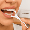 A person using a white dental floss pick, showcasing their teeth and maintaining oral hygiene.