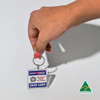 A hand holding a square acrylic keychain featuring a design in blue and white, with a logo.