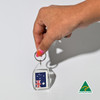 A hand holds a clear tear drop acrylic keychain featuring the Australian flag. The keychain has a silver ring and a logo.