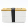 A two-layer lunch box in white with a bamboo lid, secured by a black strap. It features a logo on the top.
