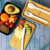A two-layer lunch box in black and tan, featuring a variety of fresh ingredients and utensils on a wooden board.
