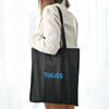 A black shopping tote bag with a V gusset, featuring a logo, held by a person against a light backdrop.