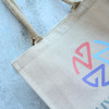 A jute tote bag in a natural colour with a multi-coloured logo design and sturdy handles.