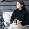 A black Zen mirror finish mug with a logo, held by a woman sitting on a couch with a blanket.