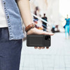 A black magnetic wireless power bank is attached to a smartphone held in a person's hand, with a blurred background.