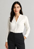A white long sleeve blouse with a collar, worn by a woman, paired with dark trousers. Branding is present.