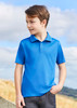 A blue short sleeve polo shirt on a young boy, standing outdoors with a scenic background. The shirt has a logo.