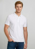 A white men's short sleeve polo shirt with a logo, paired with denim jeans.