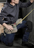 A person kneeling, wearing denim jeans and a dark hoodie, with a tool belt and a measuring tape.