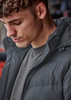 A close-up of a man wearing a dark grey hooded puffer jacket, featuring a zippered front and a casual look.