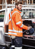 A unisex hi-vis orange softshell jacket with reflective strips, worn by a person holding tools.