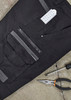 A pair of black work pants featuring multiple pockets, a zipper, and a branding logo. Tools are placed beside them.