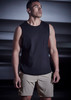A man wearing a black sleeveless top and beige sports shorts stands in a dimly lit setting. The shorts feature a logo.