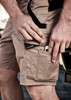 Men's streetwear shorts in khaki, featuring multiple pockets and a logo, worn by a man with one hand adjusting a phone.
