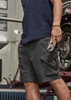 Men's rugged stretch shorts in dark grey, featuring cargo pockets and a sleek design, held by a person with a tool.
