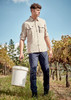 A long-sleeve, button-up shirt in beige, worn with navy pants, against a vineyard backdrop. Features a logo.