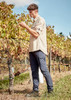A light beige long sleeve button-up shirt is worn by a man in a vineyard, paired with navy pants.