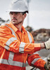 Hi-vis orange long sleeve work shirt with reflective tape, worn by a male worker in a construction setting, wearing safety gear.