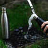 A drink bottle featuring a sleek black design, alongside a stainless steel bottle and two smaller containers on grass.
