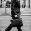 A black laptop bag carried by a person in a suit, featuring a sleek design and a handle.