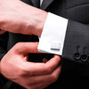 Silver plain cufflinks attached to a white dress shirt's cuff, worn with a black suit jacket.