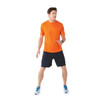 An orange short sleeve tech tee is worn by a man paired with dark shorts and blue athletic shoes. The shirt has a logo.