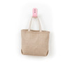 A herringbone jute tote bag in beige with light-coloured handles, hanging on a pink hook.