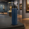 A drink bottle with a sleek navy blue finish and a black lid, positioned on a surface in an art gallery setting.
