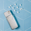 A slider tin containing sugar-free breath mints alongside several white mints scattered on a blue textured background.