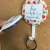 A round button badge with a vibrant fruit design, attached to a keyring and featuring a white pull tab.