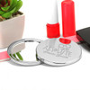 A compact mirror with a shiny silver finish, placed beside a small potted plant and red nail polish.