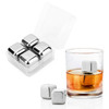 A drink bottle sits beside a glass containing amber liquid and shiny silver whiskey ice cubes in a transparent case.